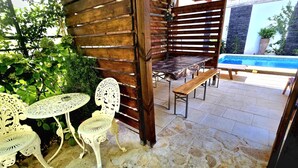 An outdoor patio with stone flooring, a wooden pergola, a pool, and white metal chairs. - Apartment Rustica Zadar with exclusive use of pool & yard (Zadar)