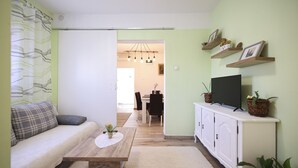 A living room with a sofa, coffee table, TV, and shelving with plants. - Apartment Rustica Zadar with exclusive use of pool & yard (Zadar)