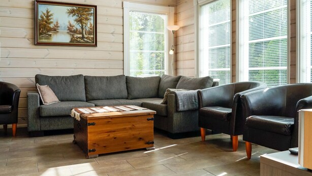 Un salon chaleureux avec un plafond en bois, un ensemble de canapés gris, une table basse en bois et un tableau représentant un paysage.