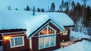 Une cabane en bois avec un toit enneigé, de grandes fenêtres et une cheminée.