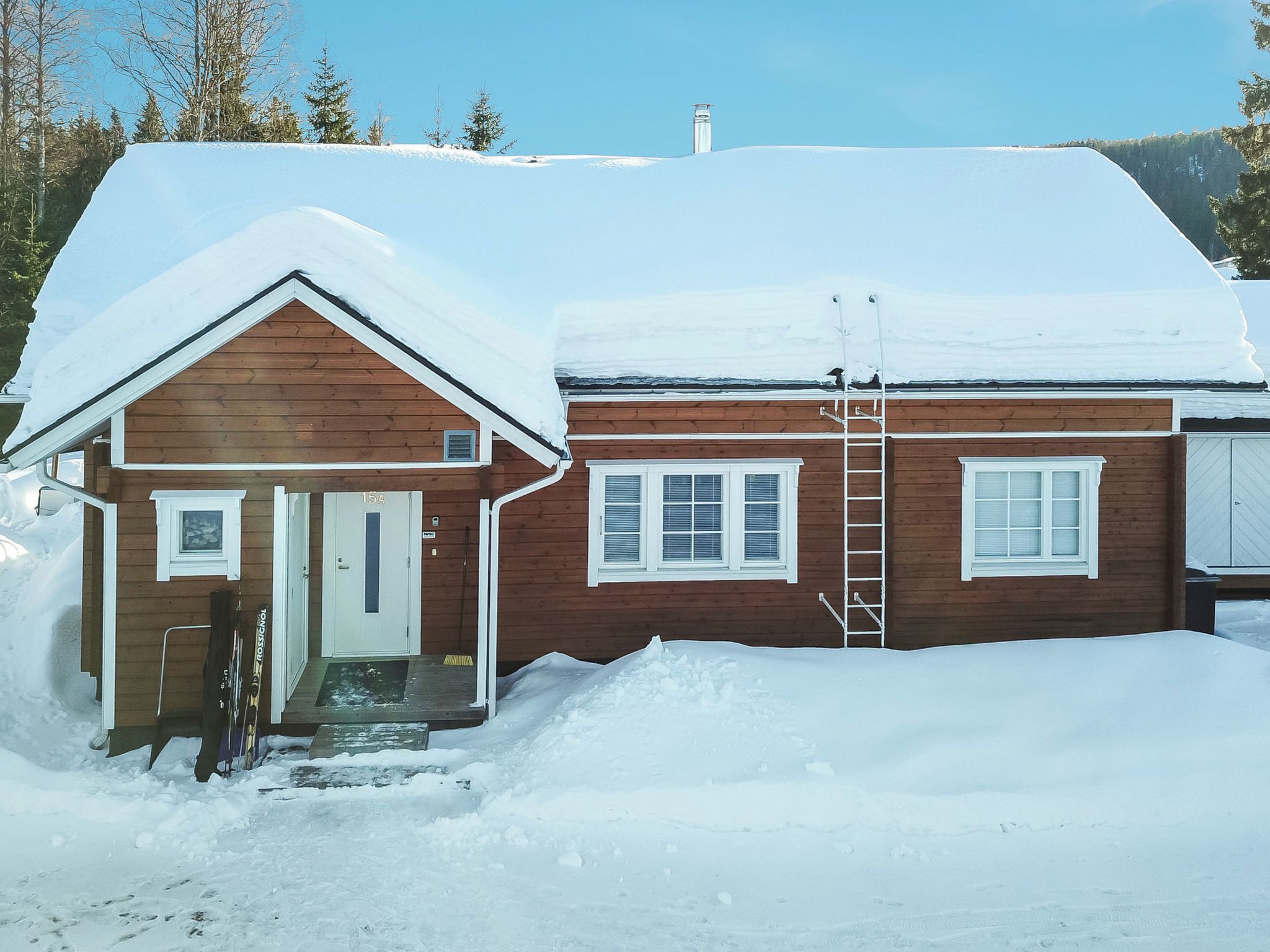 A wooden cabin with a snow-covered roof, a door, and a window.