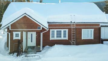 A wooden cabin with a snow-covered roof, a door, and a window.
