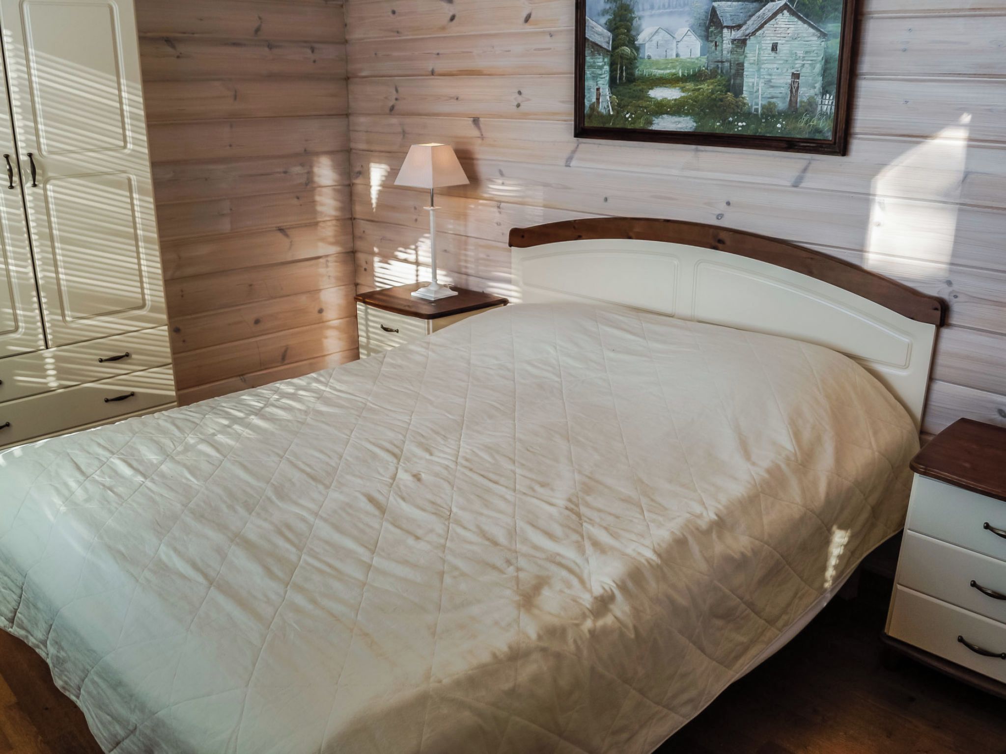 A bedroom with a bed, a nightstand, a lamp, and a wooden wall.