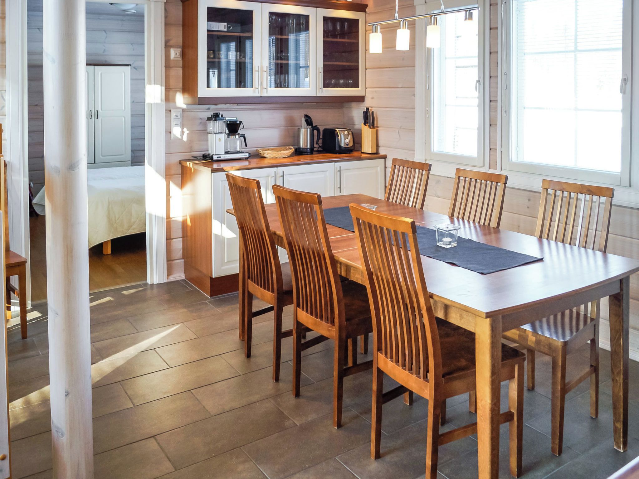 Una cocina moderna con armarios blancos, una mesa de comedor con sillas de madera y vistas al exterior a través de ventanas amplias.