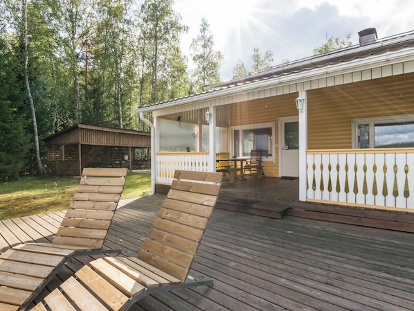 A wooden deck with lounge chairs, a covered patio area, and a view of a forested area.