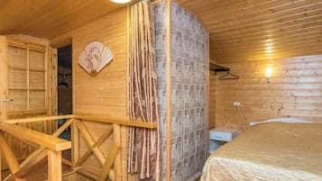 A wooden interior with a bed, a bathroom with a shower, and a small desk.