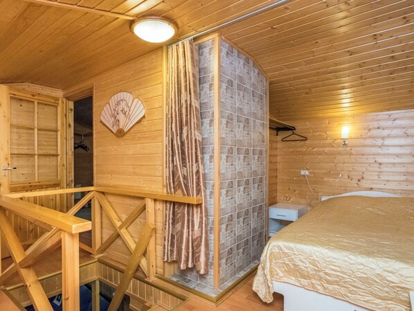 A wooden interior with a bed, a bathroom with a shower, and a small desk.