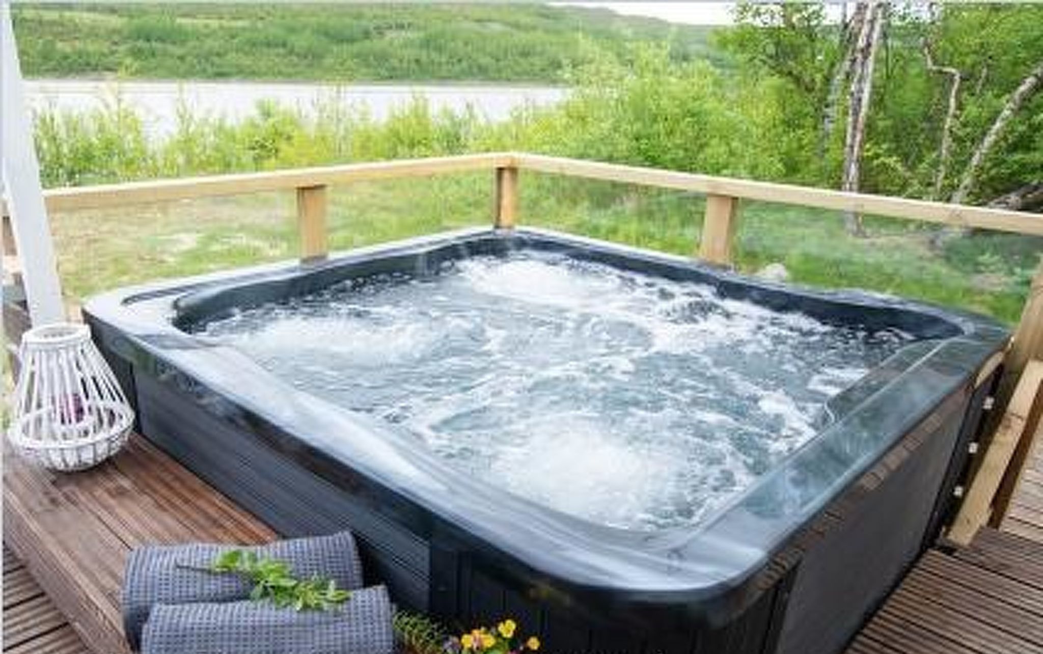 A hot tub on a wooden deck with a view of a lake and greenery.