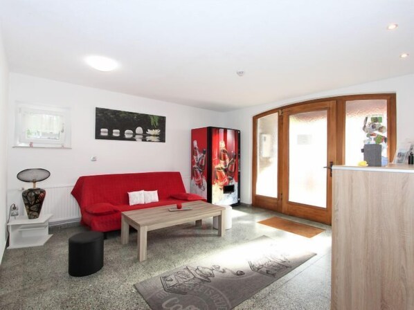 A modern living room with a red sofa, a wooden coffee table, and a large painting. There is a small side table with a lamp and a black ottoman.