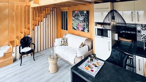 A modern interior with a staircase, a sofa, a dining table with glasses, and a kitchen area.