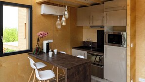 A modern kitchen with a wooden ceiling, a dining area with a dark island, and a view of greenery outside.