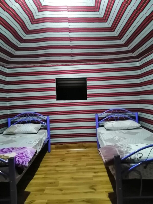 A room with two beds, a small window, and a wooden floor.