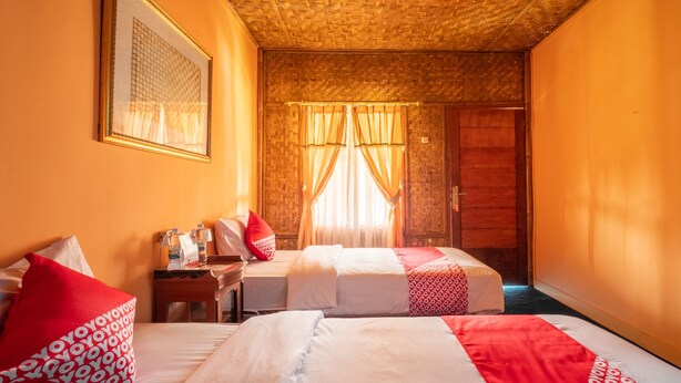 A room with two beds, each with white and red bedding, a wooden headboard, a small table with a lamp, and a framed picture on the wall. - OYO 644 Grand Yustik Selabintana (Sukabumi)
