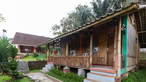 A wooden house with a porch, steps leading to the entrance, and a small brick structure in front. - OYO 644 Grand Yustik Selabintana (Sukabumi)