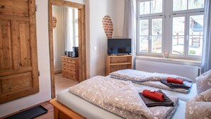 Ein Schlafzimmer mit zwei Betten, einer hölzernen Kommode, einem Fernseher auf einem Tisch und einem Fenster mit Blick ins Freie.