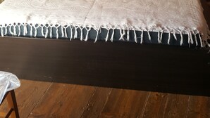 Un lit avec une tête de lit sombre, une couvre-lit blanche et un plancher en bois.
