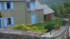 Une maison à deux étages avec des volets bleus, un mur en pierre et une cour gazonnée.