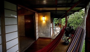 A wooden interior with a hammock, a wall-mounted light, and a view of greenery outside. - Finca Maresia (Drake Bay)