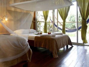 A room with two beds, a large window with curtains, and a hammock outside. - Finca Maresia (Drake Bay)