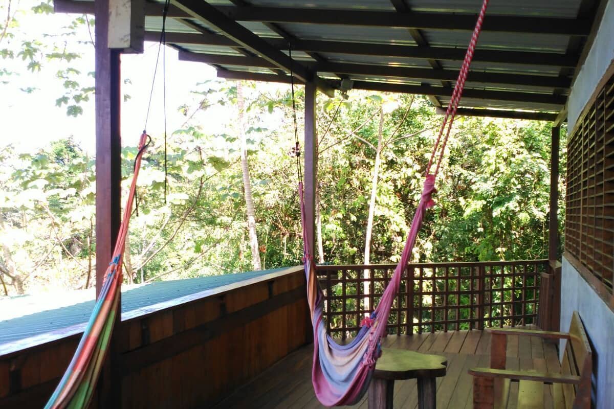 A wooden deck with a hammock, a bench, and a view of the forest.