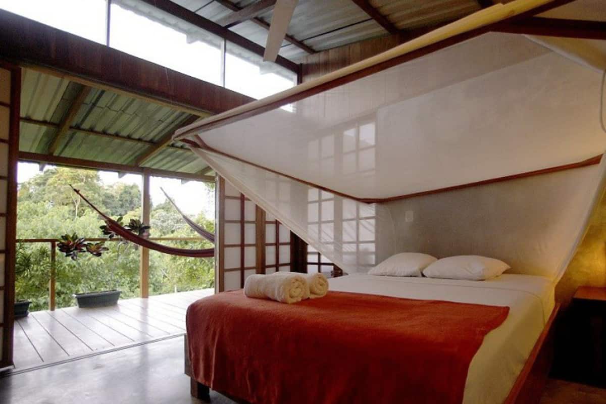 A bedroom with a bed, a hammock, and a view of greenery.