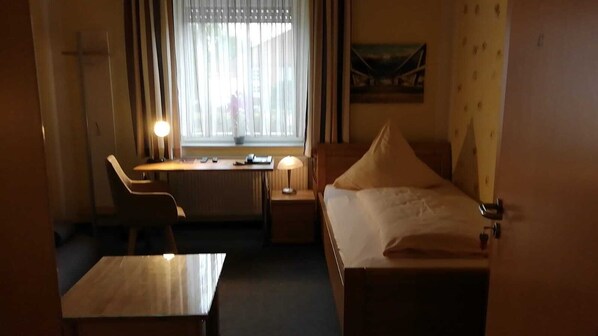 A hotel room with a bed, a desk, a chair, a lamp, and a window with curtains.