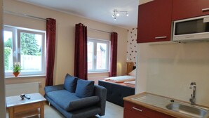 A compact room with a sofa, a small table, a bed, a TV, and a kitchenette. - Hotel Landhaus Effeld (Wassenberg)
