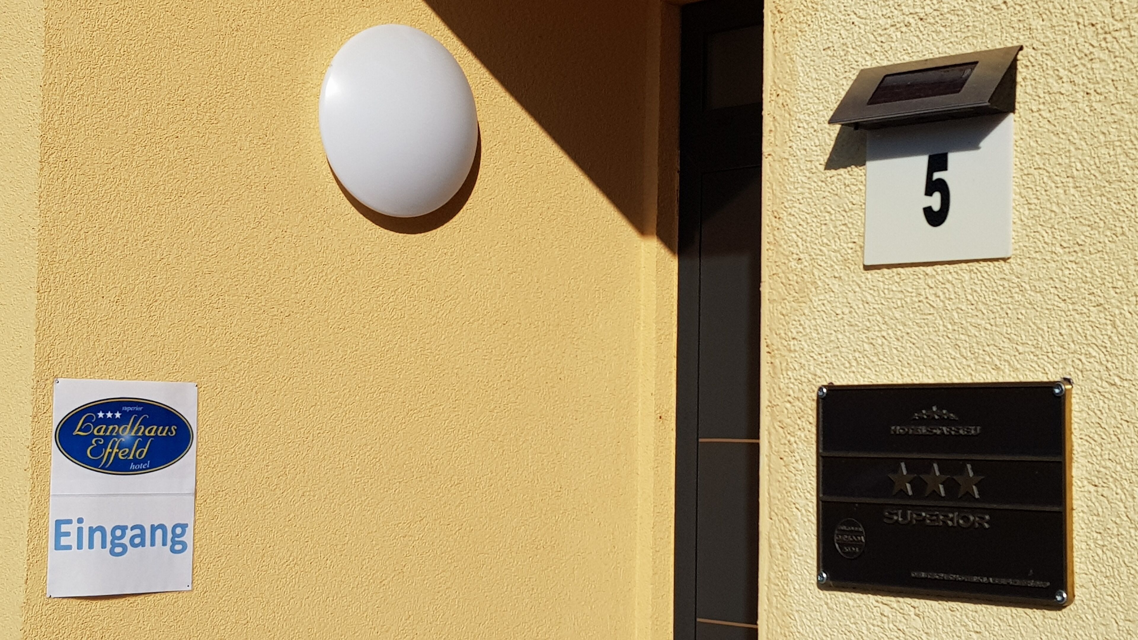 La façade d’un immeuble, avec une enseigne indiquant l’hôtel Bandhaus Effeld, une boîte aux lettres portant le numéro 5 et un cadre de porte.