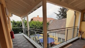 A covered balcony with a tiled floor, metal railing, and a view of a neighboring building with a red roof. - Hotel Landhaus Effeld (Wassenberg)