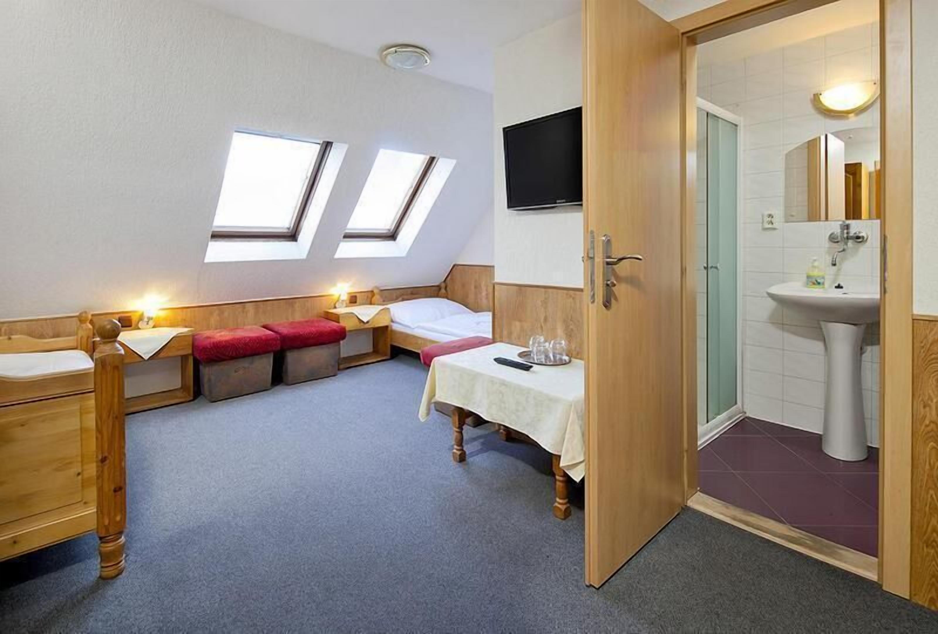 Une chambre de taille modeste, comprenant un lit, une petite table, un téléviseur et une salle de bain avec un lavabo et un miroir.
