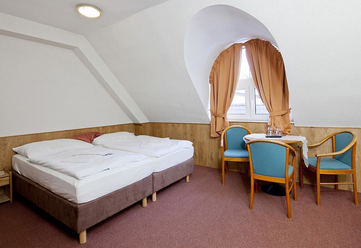 A room with a bed, two chairs, a small table, and a window with curtains.