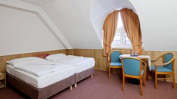 A room with a bed, two chairs, a small table, and a window with curtains.