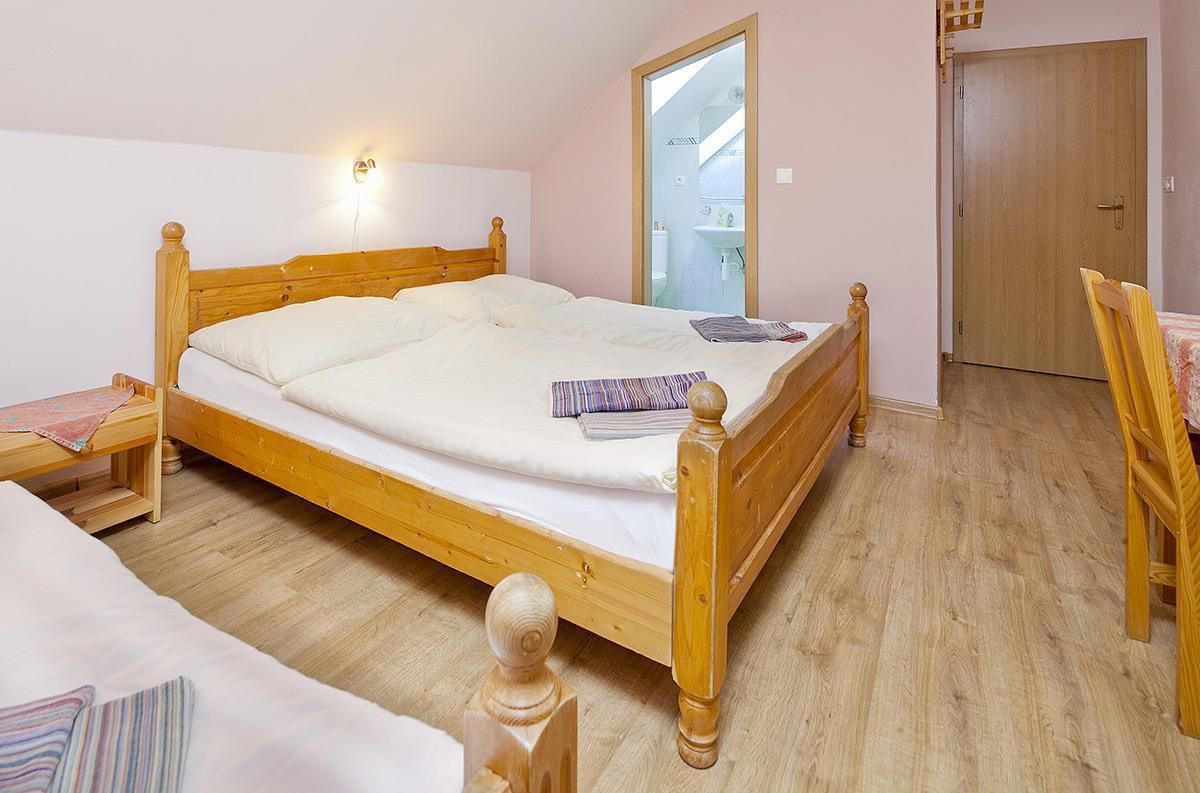A wooden bed in a room with a wooden floor, a wooden chair, and a door.