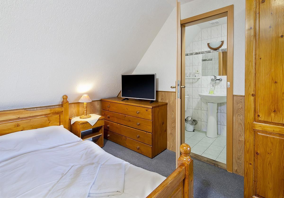 Un dormitorio con cama, cómoda de madera, televisor y baño visible a través de una puerta abierta.