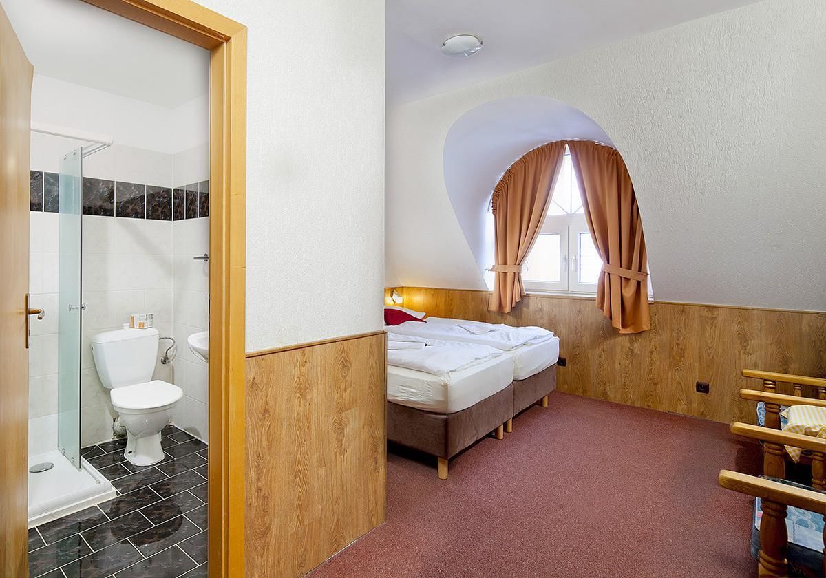 Habitación de hotel con ducha, inodoro, cama y ventana con cortinas.