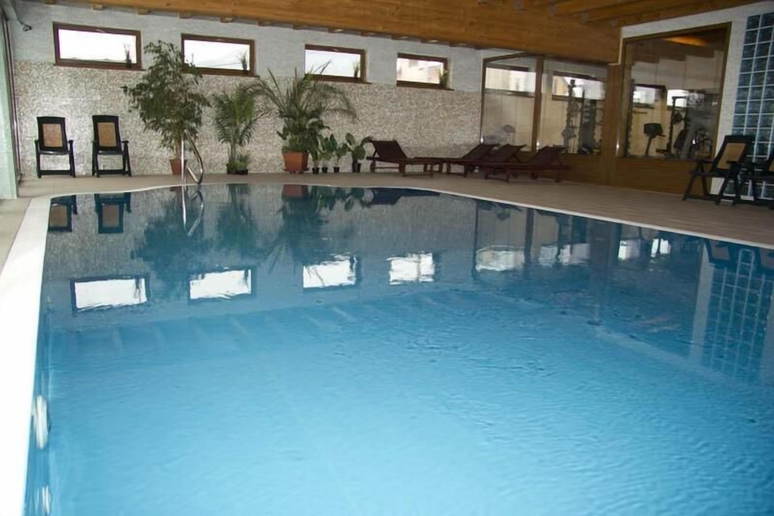 Une piscine intérieure à l’eau claire, entourée de chaises longues et de plantes en pot.