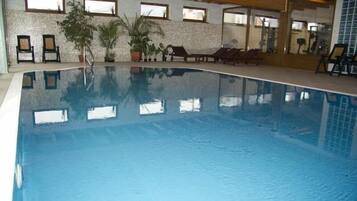 Une piscine intérieure à l’eau claire, entourée de chaises longues et de plantes en pot.