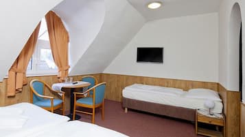 A hotel room with a bed, a desk with two chairs, a TV mounted on the wall, and a window with curtains.