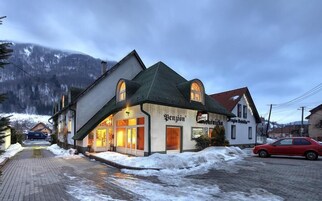 A traditional building with a sign 'Benzión' and 'Proquichka' on the facade, located in a snowy village with a mountain backdrop.