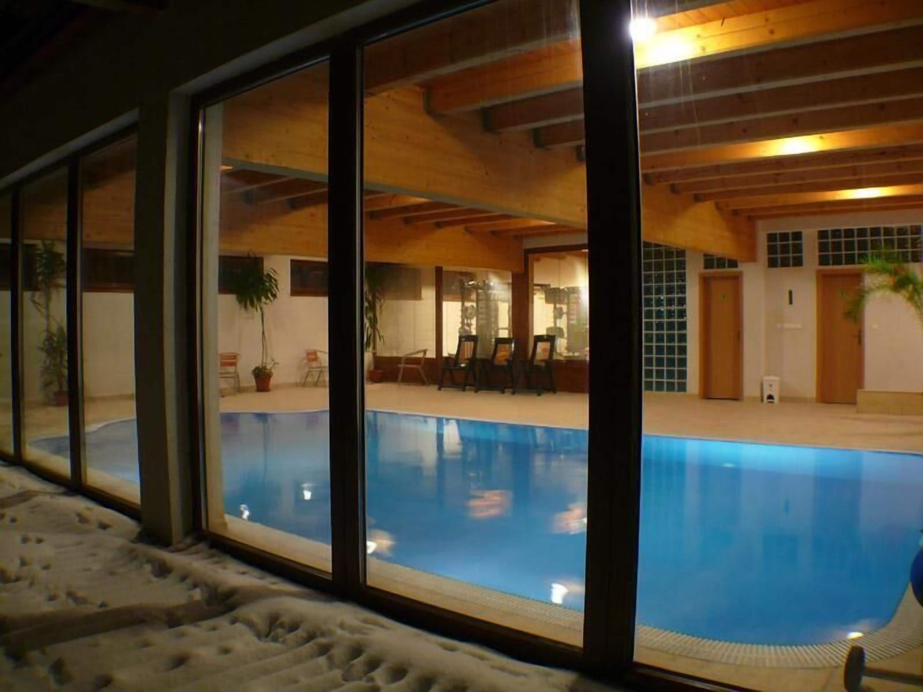 Ein Innenpool mit großen Glaswänden, Holzbalken und gefliestem Boden.