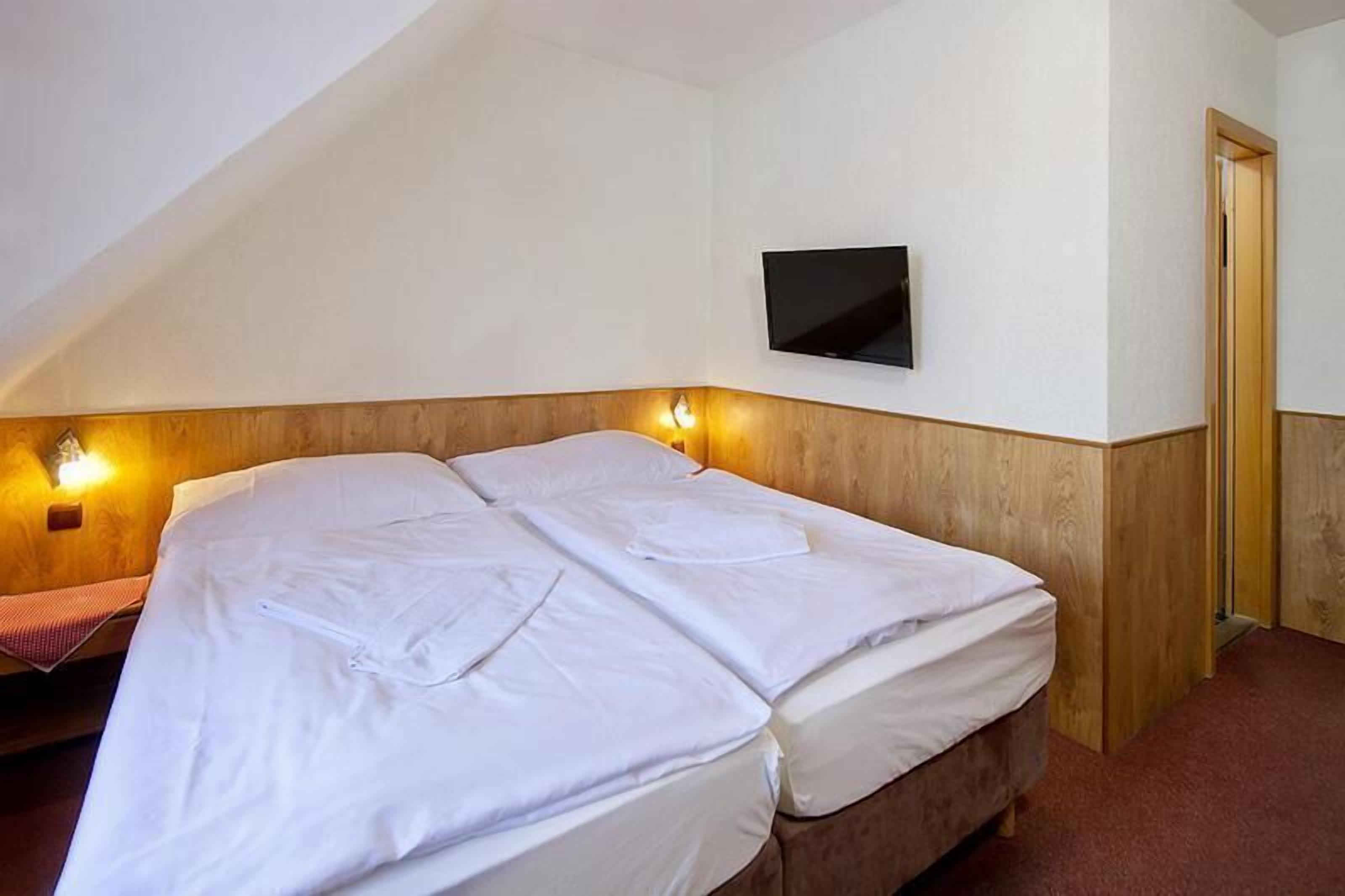 Una cama individual con ropa de cama blanca en una habitación con paneles de madera y un televisor montado en la pared.