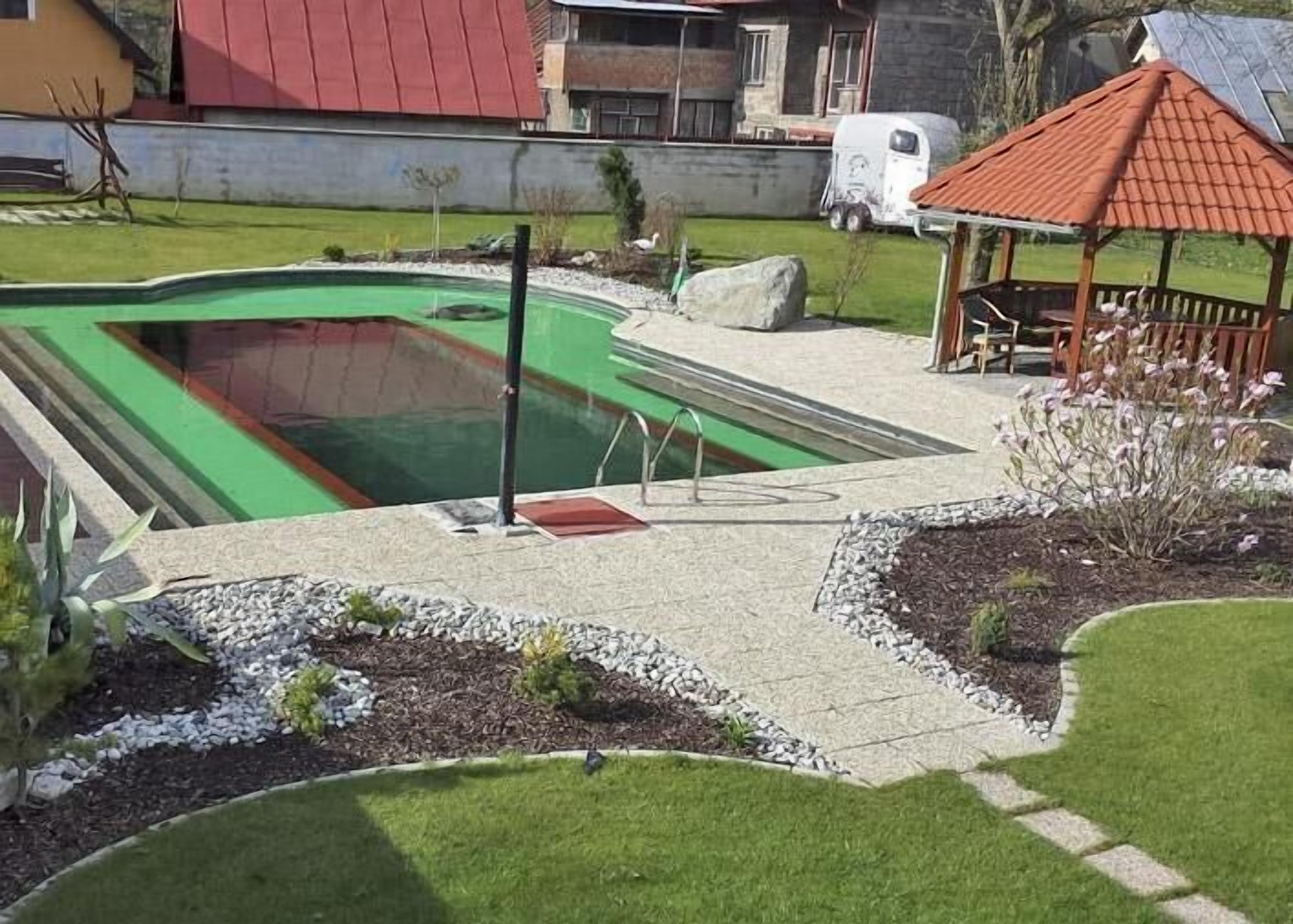 A swimming pool with a green interior, surrounded by a landscaped garden with a gazebo and a small deck.