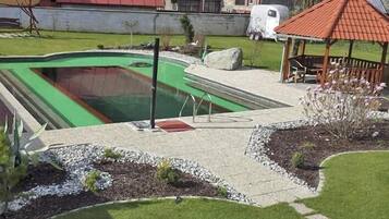 A swimming pool with a green interior, surrounded by a landscaped garden with a gazebo and a small deck.