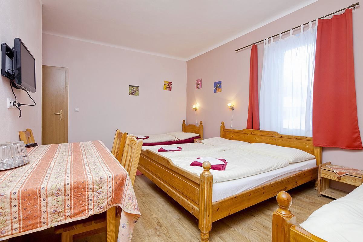A bedroom with two wooden beds, a table with a striped tablecloth, and a television mounted on the wall.