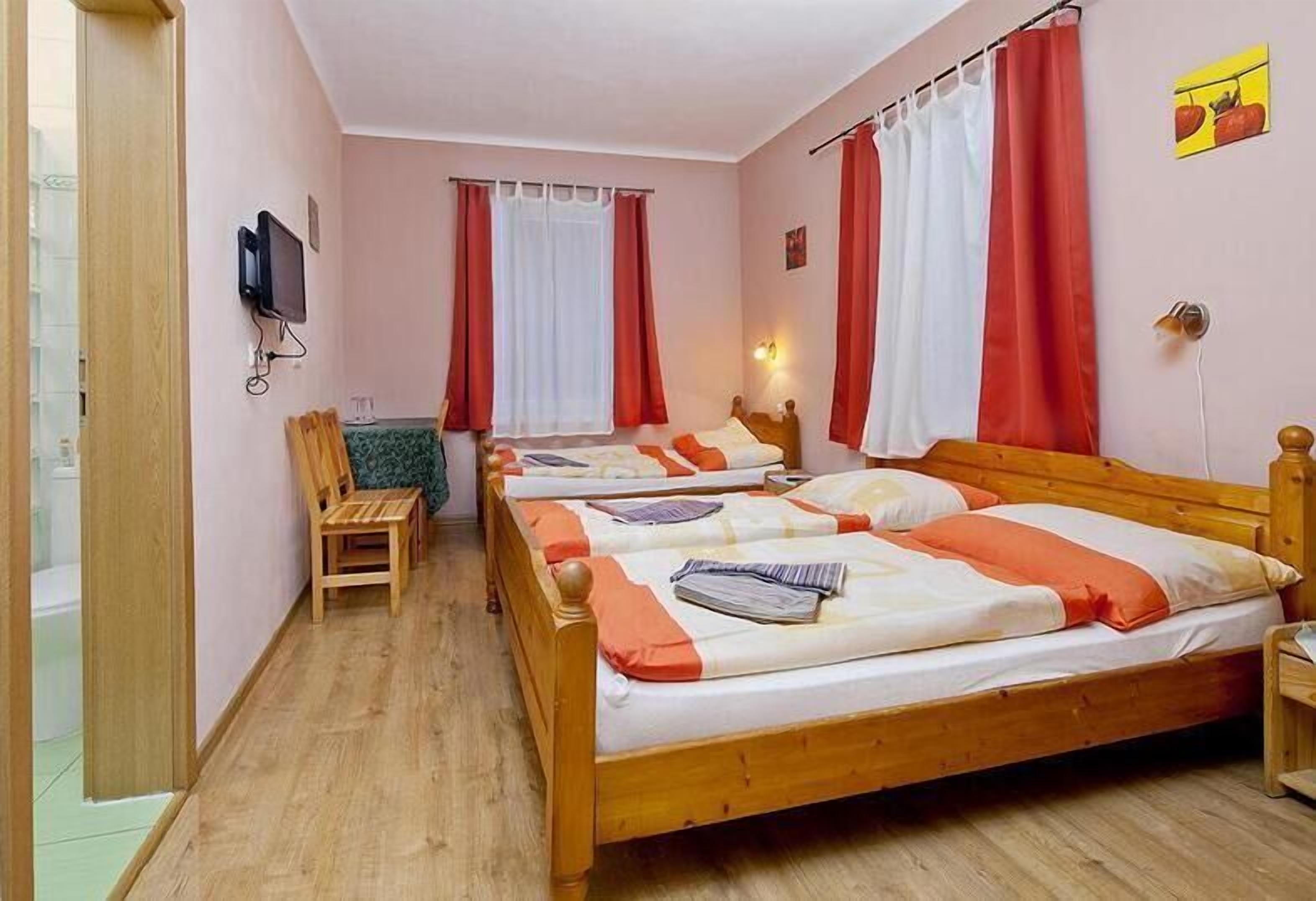 Une chambre d’hôtel avec trois lits en bois, chacun recouvert d’une couverture rouge et blanche, et une chaise en bois.