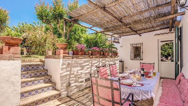 A patio with a table set for dining, surrounded by potted plants and a pergola. - Villa I Magi (Anacapri)