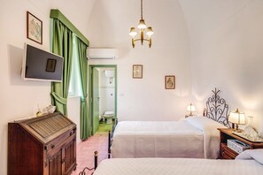 A hotel room with two beds, a television, a wooden cabinet, and a chandelier.