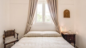 A bedroom with a bed, a wooden chair, a nightstand with a lamp, and a window with curtains. - Villa I Magi (Anacapri)
