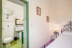 A bedroom with a bed, a bedside table with a lamp, a mirror, and a toilet in the adjacent bathroom.