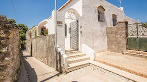 A narrow street with a white building featuring a gate, steps, and a stone wall. - Villa I Magi (Anacapri)